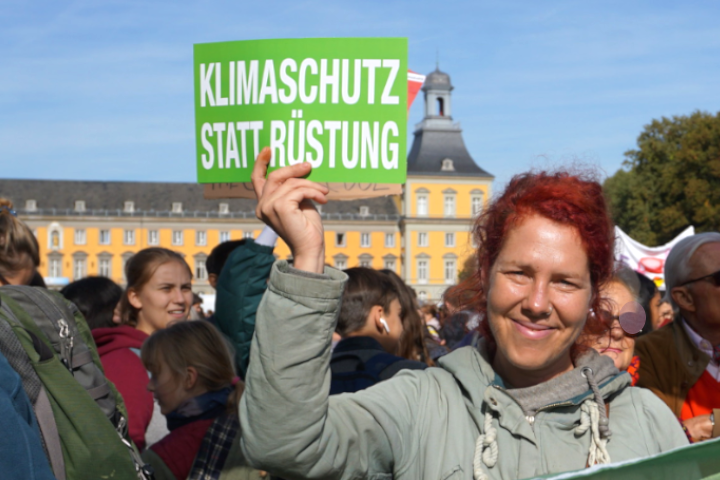 Eine Aktivistin hält bei einer Demo in Bonn ein Schild mit der Aufschrift "Klimaschutz statt Rüstung" hoch.